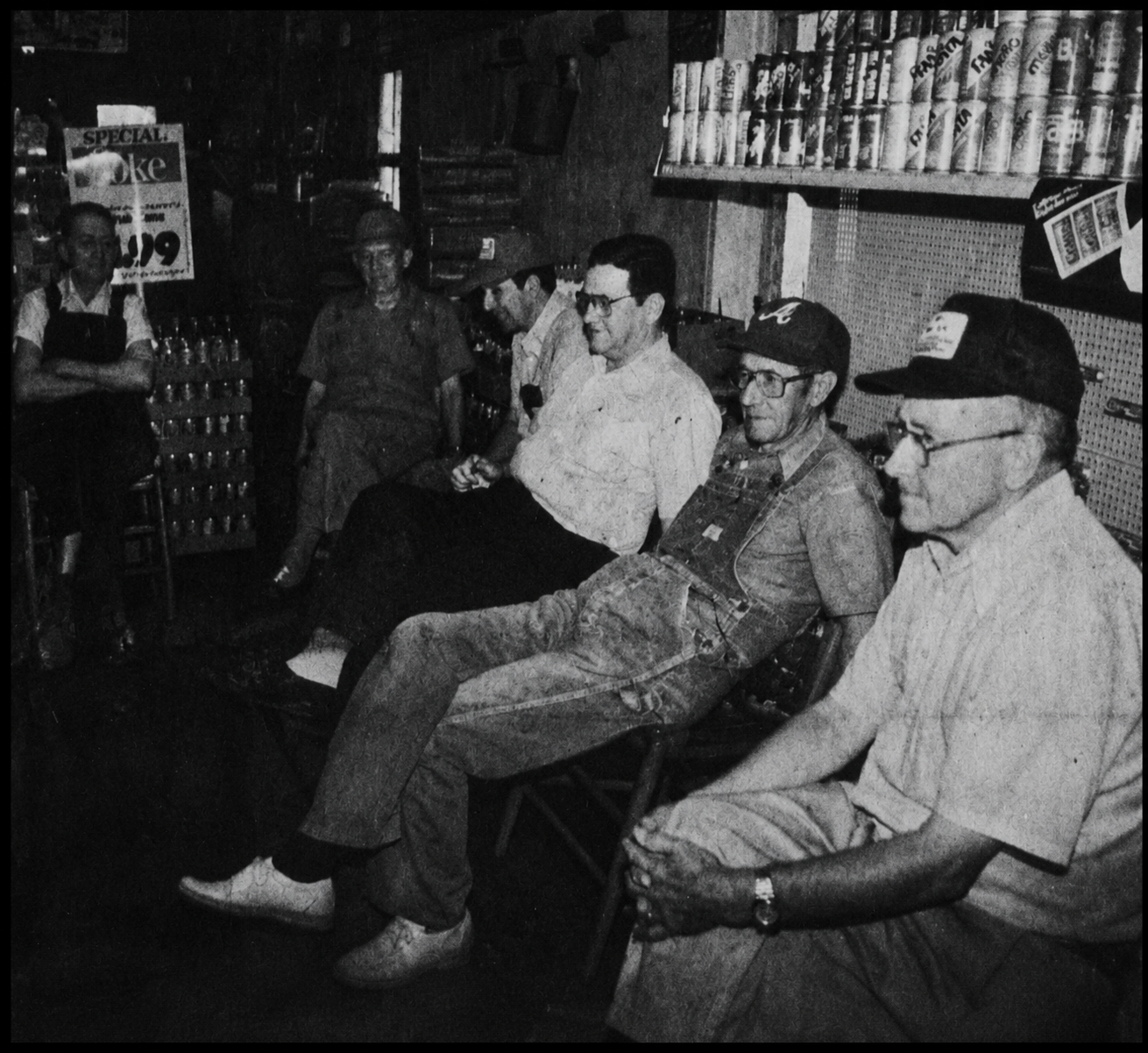 Doc Holcomb standing at far left while several men sit and talk inside his store.