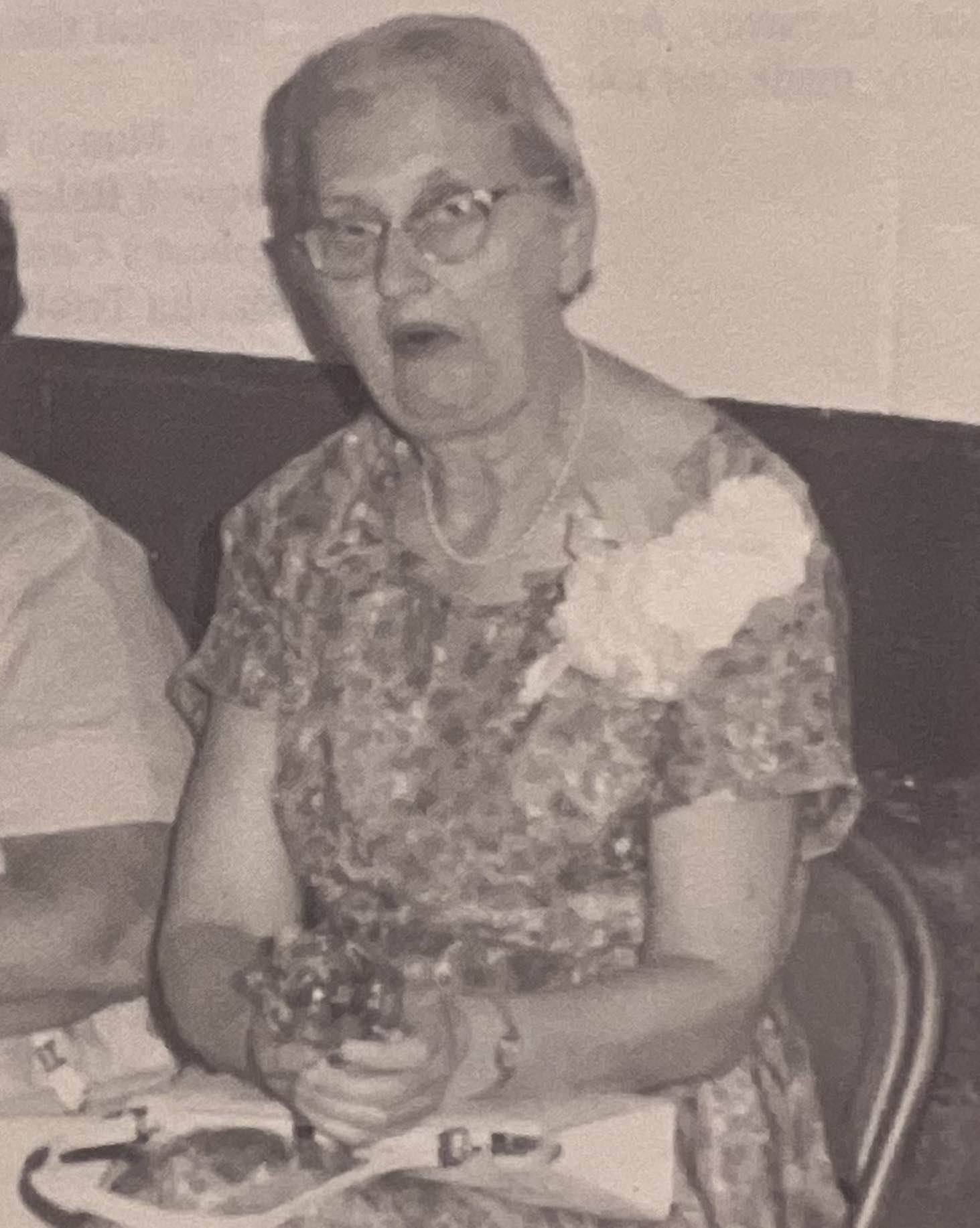 Pearl Holcomb seated at a table, wearing glasses and a corsage.